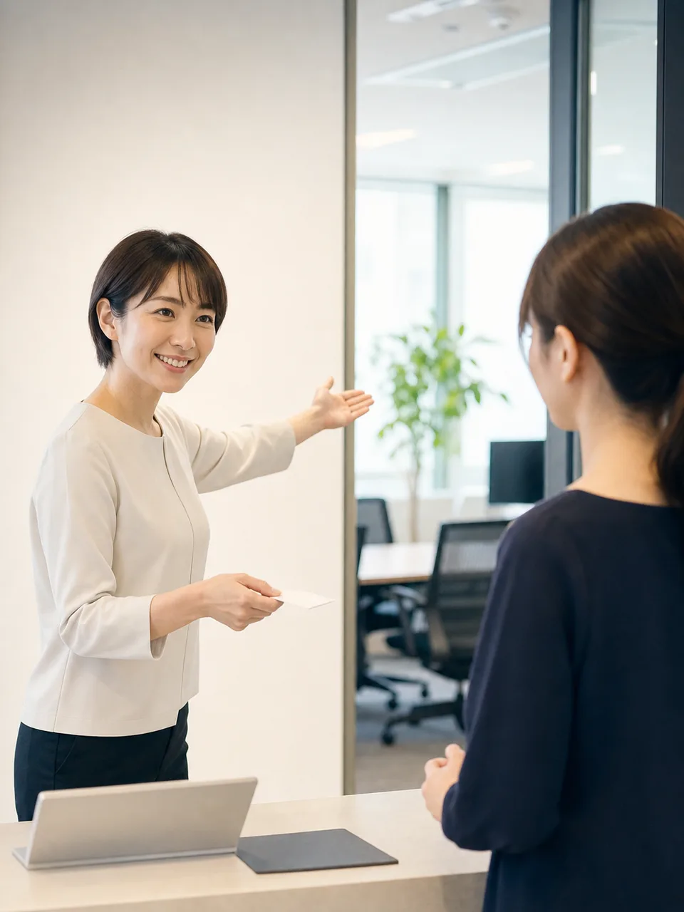 オフィスで案内する日本人受付スタッフ（自然な縦位置写真）。受付、来客対応、オフィス、接客研修の記事向け素材です。