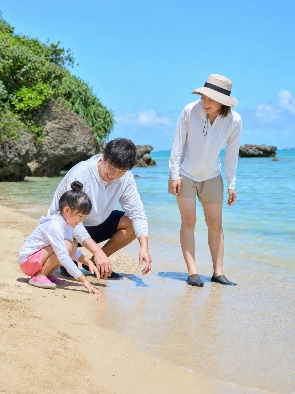 沖縄の海を楽しむ日本人家族（自然な縦位置写真）。沖縄旅行、夏休み、家族旅行、観光キャンペーン向け素材です。