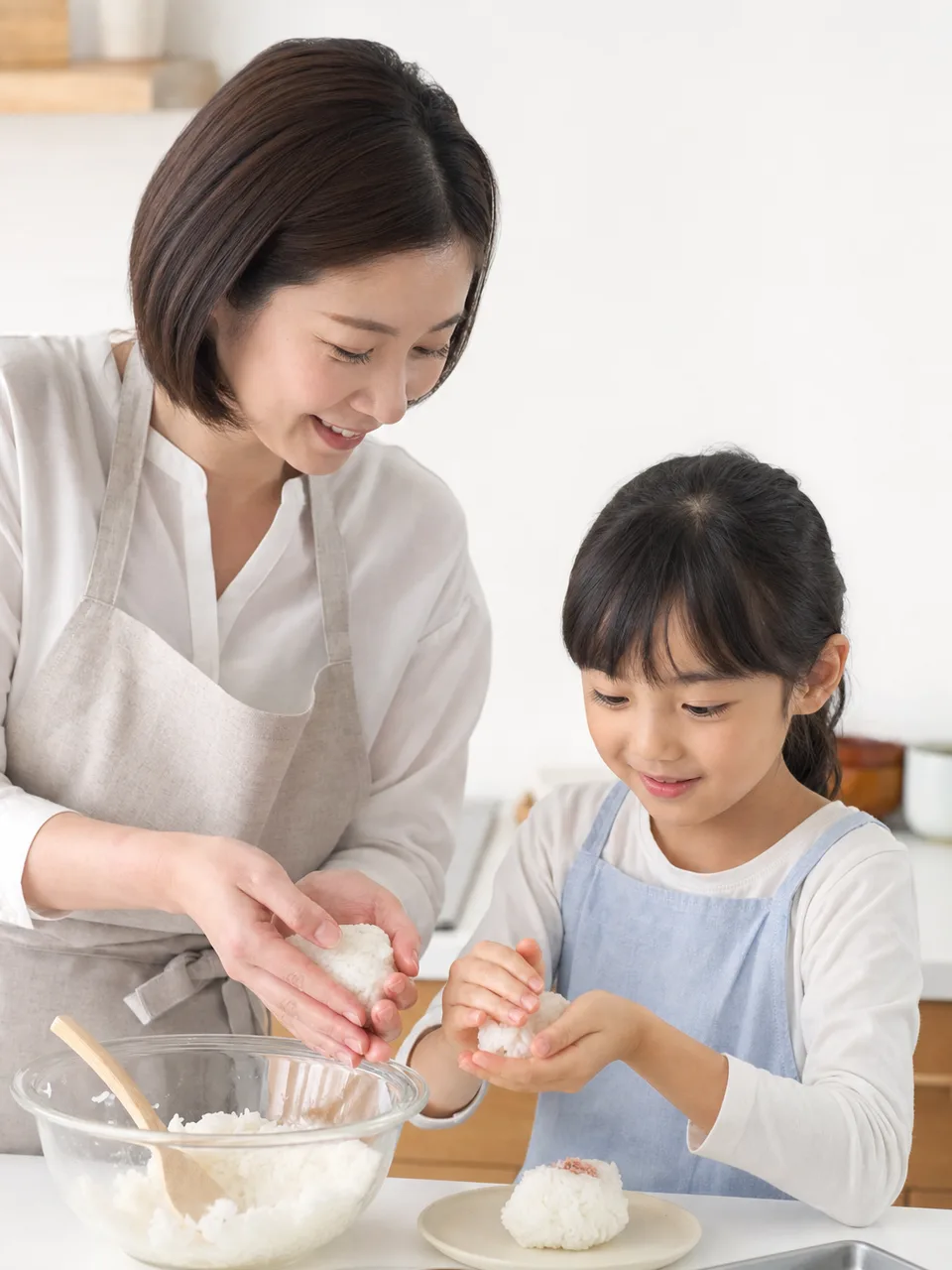 おにぎりを作る日本人親子（自然な縦位置写真）。おにぎり、家庭料理、お弁当、親子の記事向け素材です。
