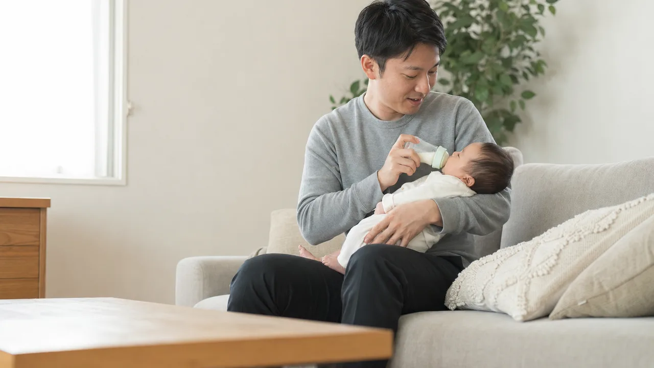 赤ちゃんを世話する日本人の父親（横長・コピースペース）。男性の育児参加、育休、家族サービスを伝えられる、父親と乳児の生活素材です。