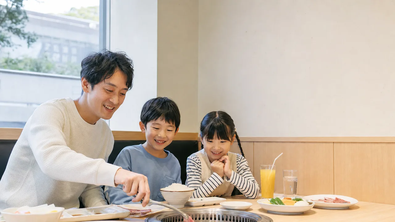 焼肉を楽しむ日本人家族（横長・コピースペース）。焼肉、家族、外食、食事の記事に使える素材です。