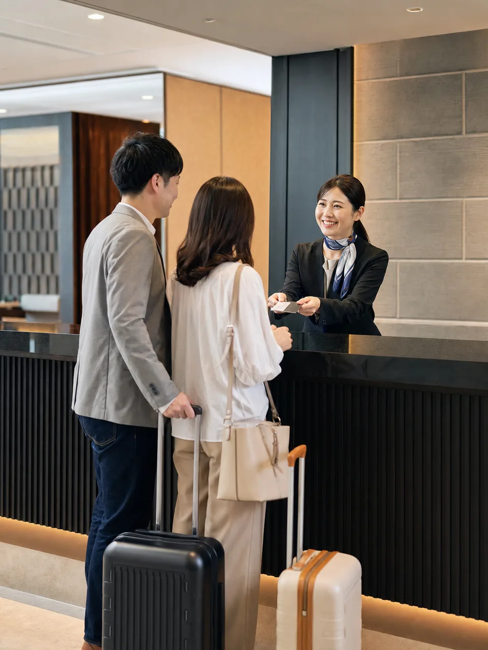 ホテルで接客する日本人スタッフ（自然な縦位置写真）。ホテル、宿泊、観光、接客サービスの記事に使える仕事素材です。