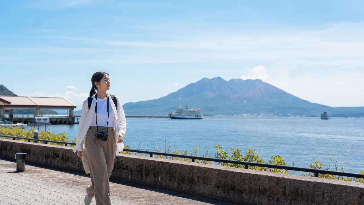 鹿児島の湾岸を旅する日本人（横長・コピースペース）。鹿児島、湾岸風景、火山、九州旅行の記事向け素材です。