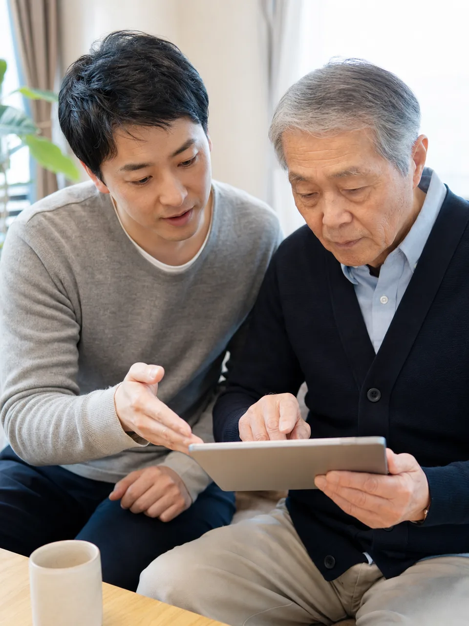 親のデジタル利用を手伝う日本人（自然な縦位置写真）。親のスマホ支援、デジタル支援、親子、高齢者の記事や案内に使える商用素材です。