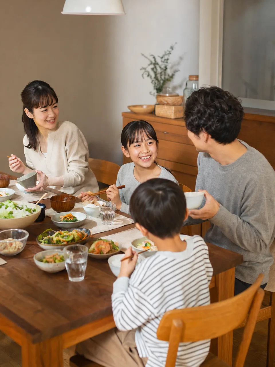 食卓を囲む日本人のステップファミリー（自然な縦位置写真）。ステップファミリー、再婚家庭、家族の食卓、子育ての記事や案内に使える商用素材です。