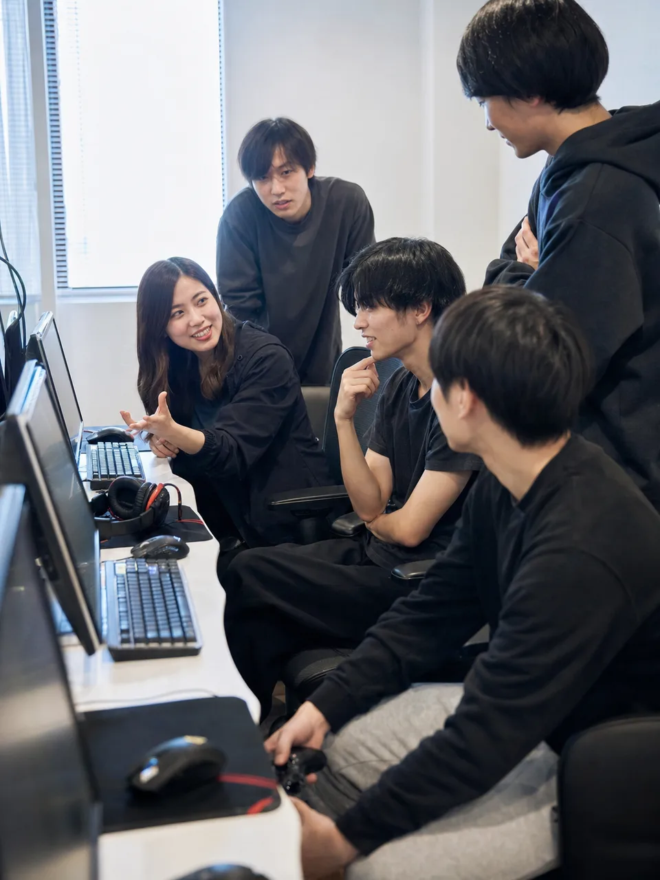 eスポーツを練習する日本人チーム（自然な縦位置写真）。eスポーツ、ゲーム、チームワーク、デジタル人材の記事向け素材です。