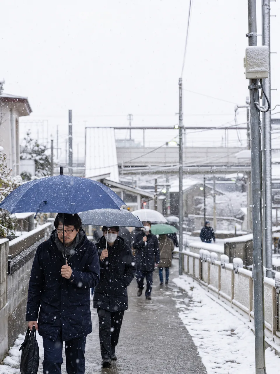 雪の日に通勤する日本人（自然な縦位置写真）。冬の交通、働き方、天候対策の記事に使える、雪の日の通勤風景素材です。