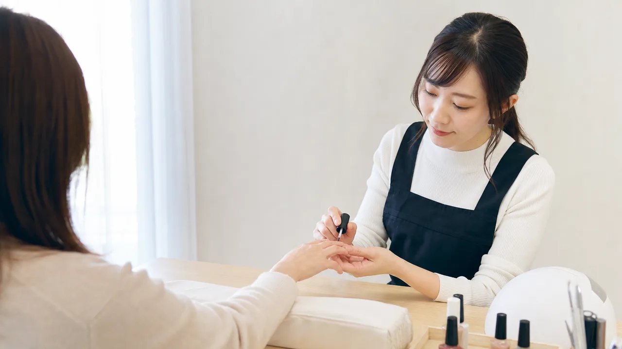 ネイルを施術する日本人ネイリスト（横長・コピースペース）。ネイリスト、ネイルサロン、美容、接客の記事向け素材です。