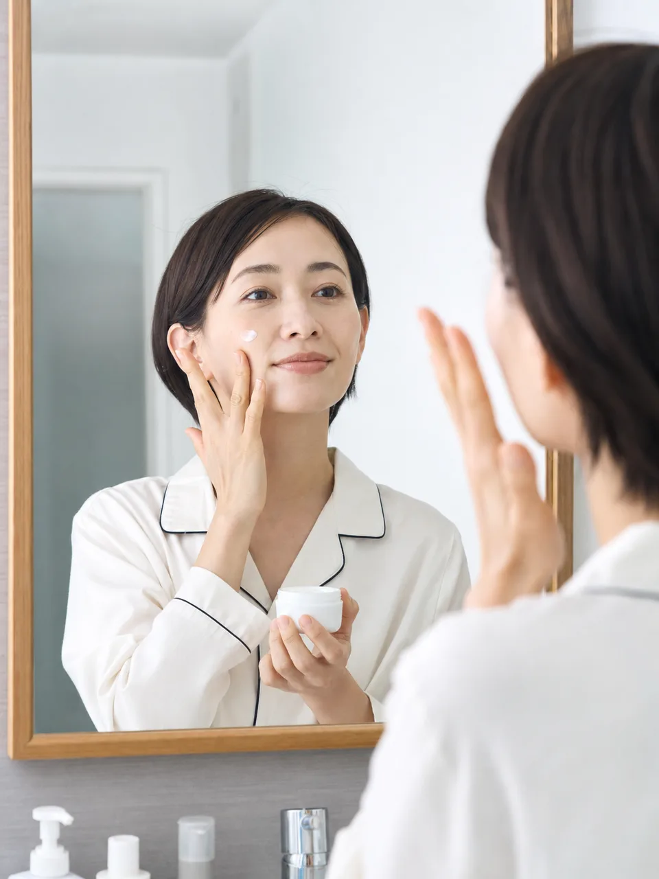 自宅でスキンケアをする日本人（自然な縦位置写真）。スキンケア、美容、セルフケア、化粧品の記事に使える清潔感のある素材です。