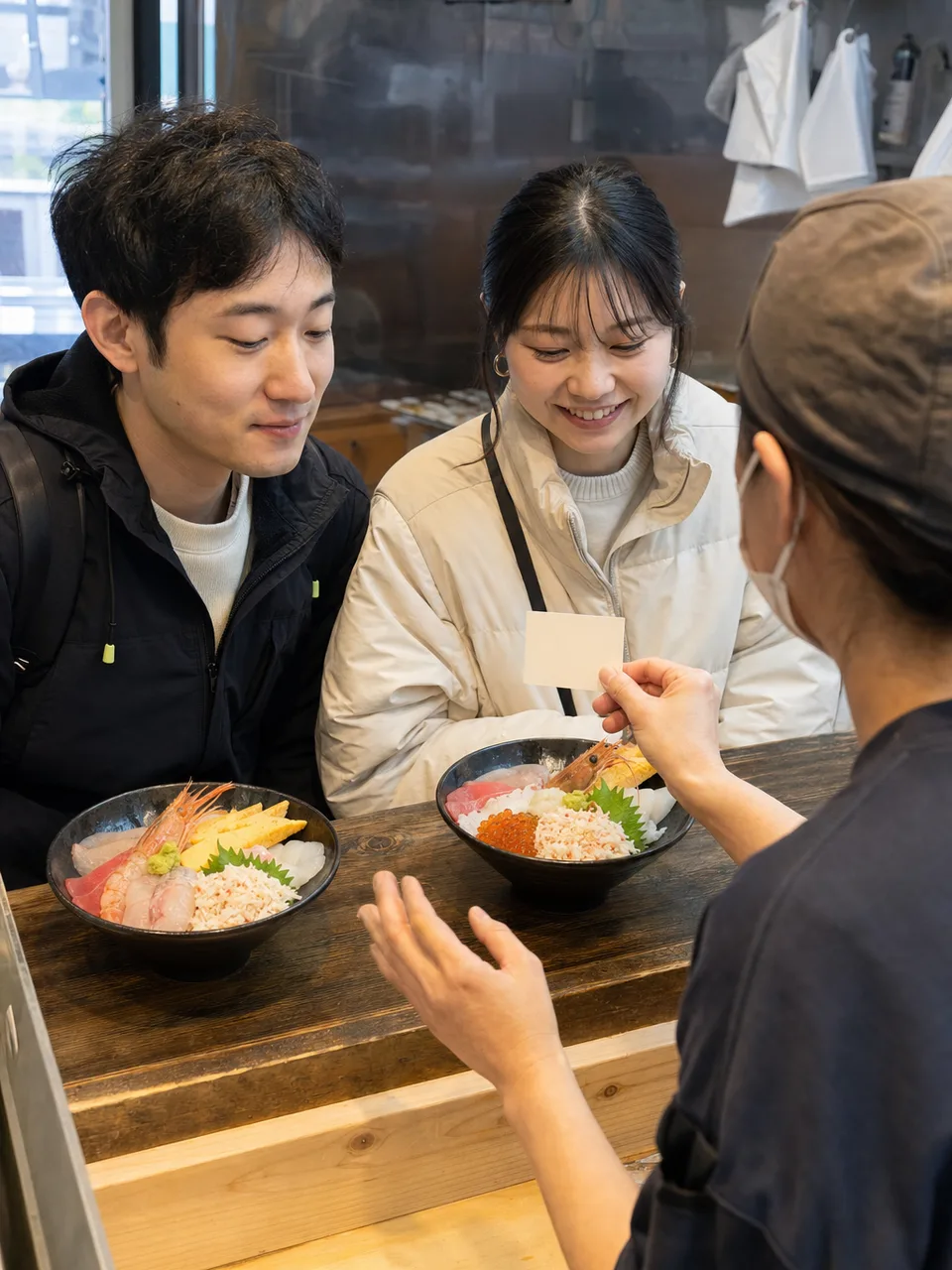 海鮮丼を味わう日本人旅行者（自然な縦位置写真）。海鮮丼、魚介、地域の食、旅行の記事向け素材です。