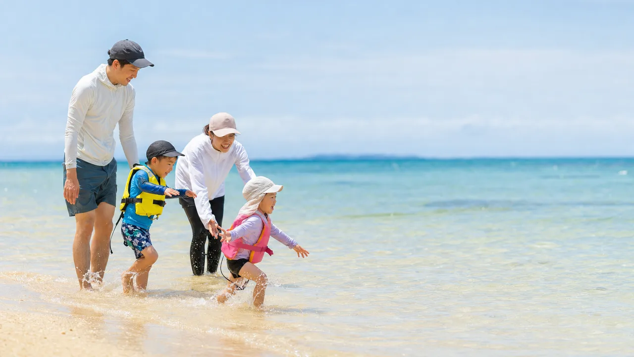 海水浴を楽しむ日本人家族（横長・コピースペース）。海水浴、夏休み、家族旅行、海の安全啓発に使える素材です。