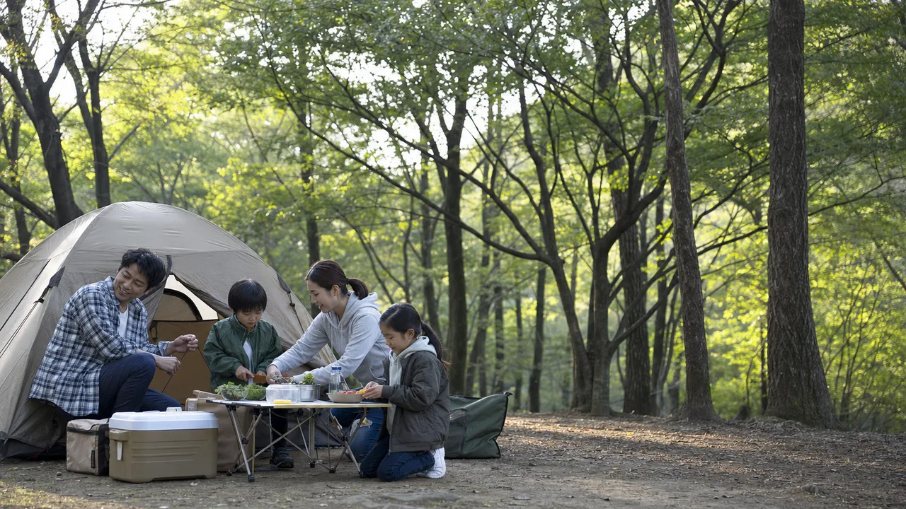 キャンプを楽しむ日本人家族（横長・コピースペース）。キャンプ、家族旅行、アウトドア用品、自然体験の記事向け素材です。