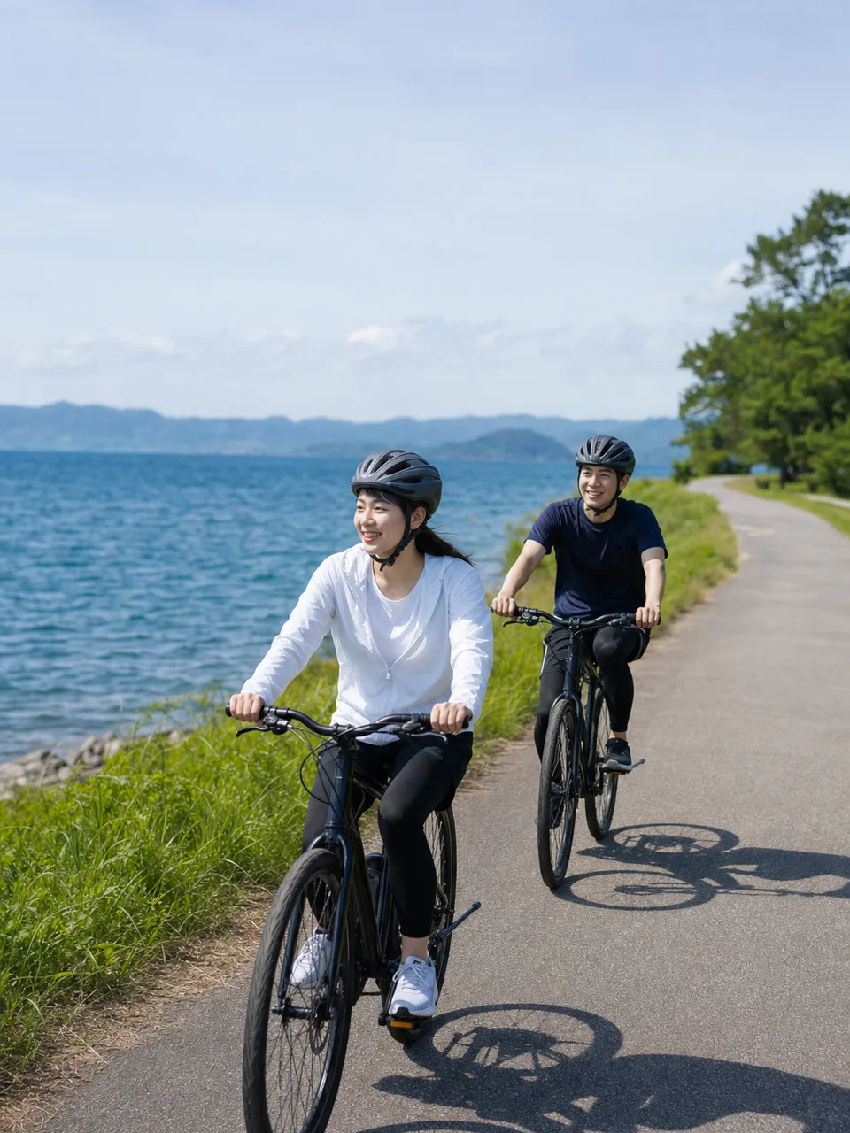 滋賀の琵琶湖畔を自転車で巡る旅行者（自然な縦位置写真）。滋賀旅行、琵琶湖、サイクリング、自転車旅行の記事や案内に使える商用素材です。