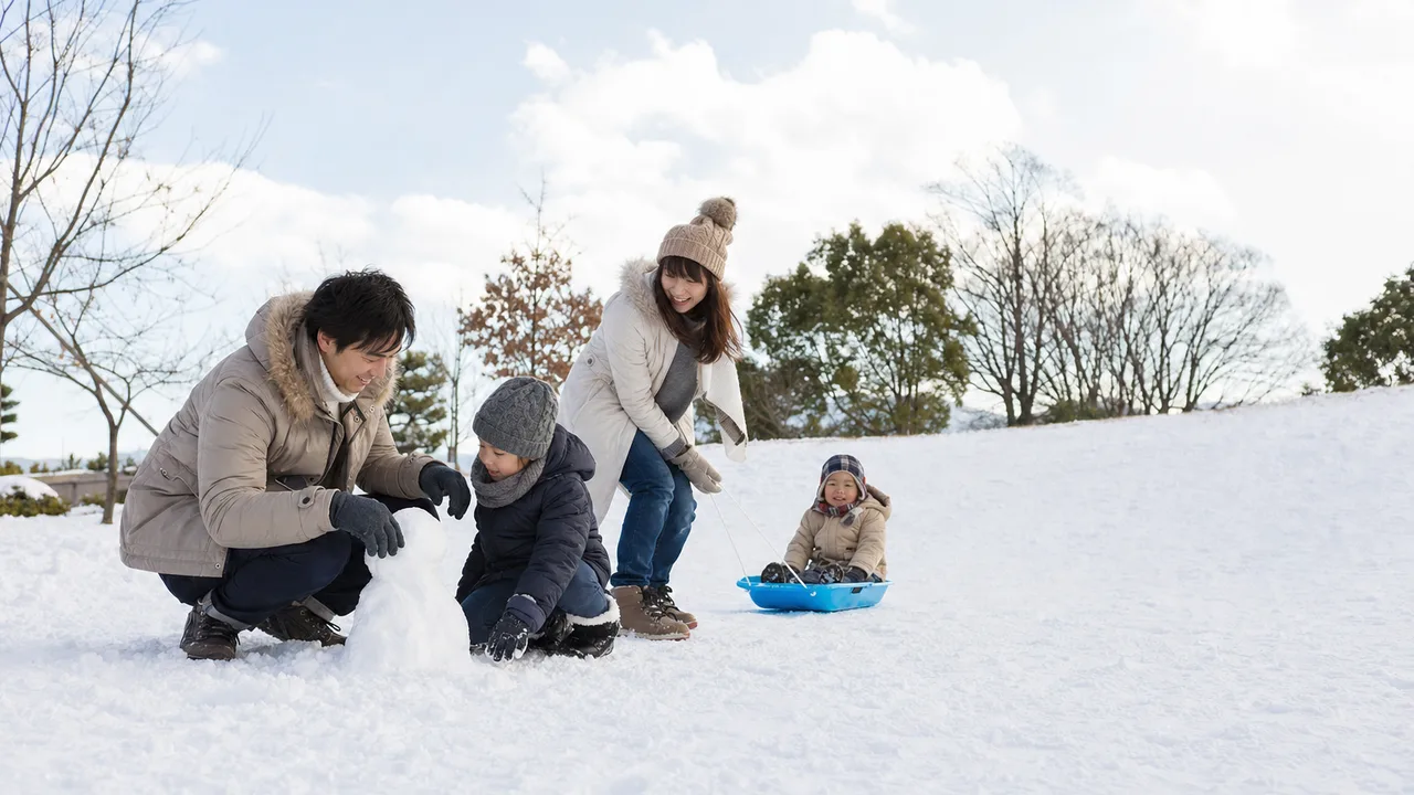 雪遊びを楽しむ日本人家族（横長・コピースペース）。雪遊び、冬、親子、屋外レジャーの記事向け素材です。
