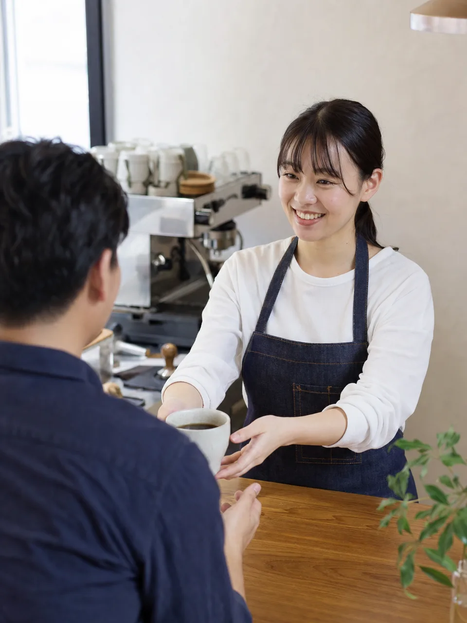 コーヒーを提供する日本人バリスタ（自然な縦位置写真）。バリスタ、カフェ、コーヒー、接客の記事向け素材です。