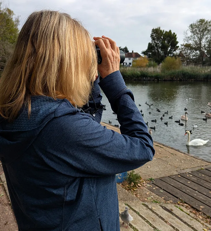 Jenny Holter, chair of SDOS, using binoculars to look out across the lake at Brooklands Park