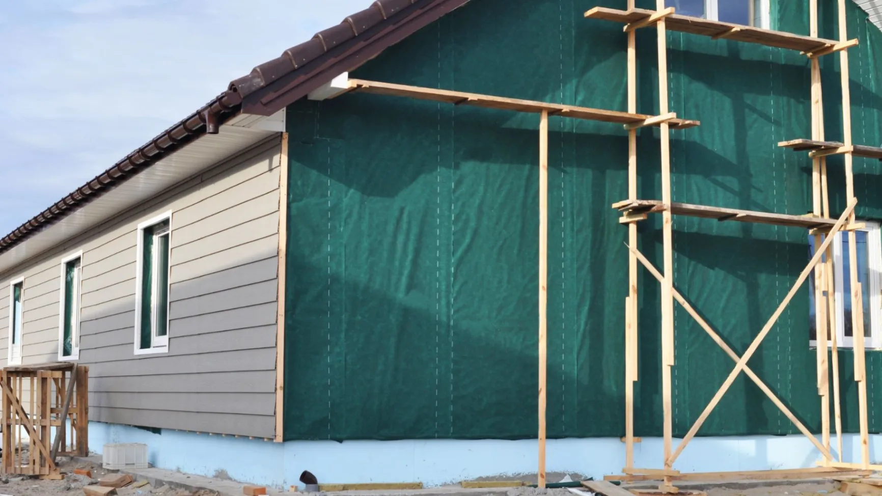 A house under construction with scaffolding and a green tarp covering part of the exterior wall.