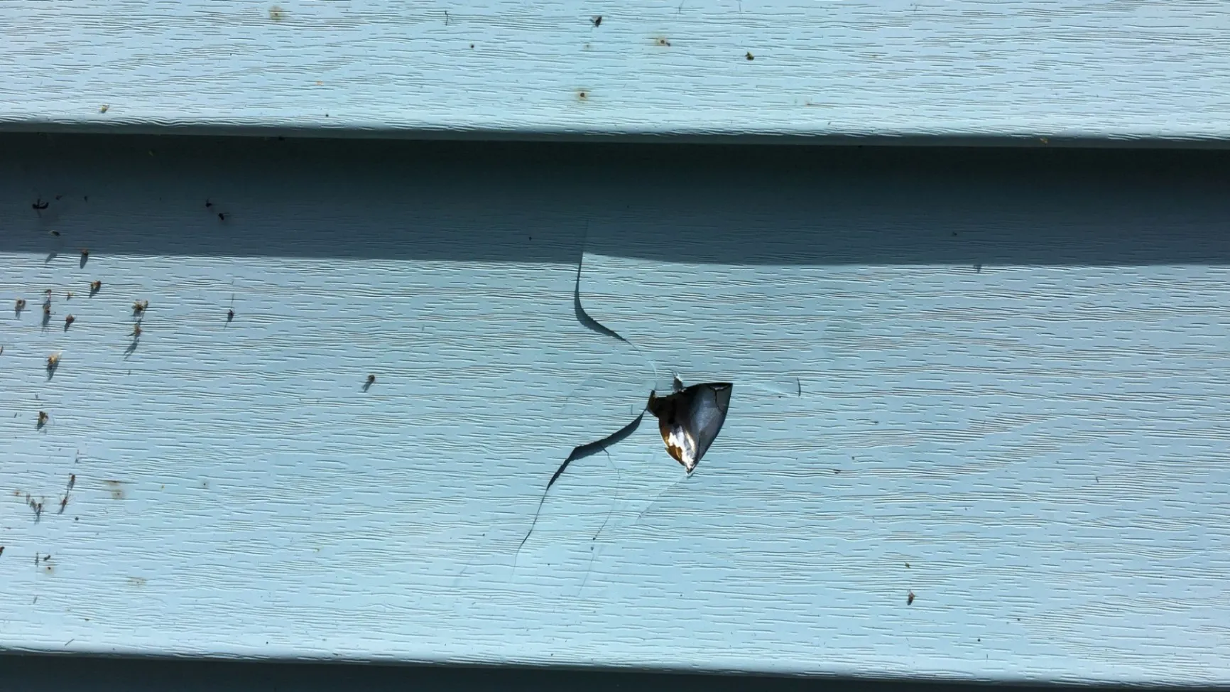 Damaged blue siding with a puncture mark and surrounding cracks."