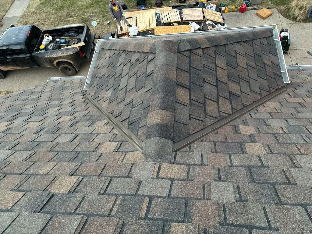 Close-up view of a newly installed asphalt shingle roof with workers and equipment on the ground below.