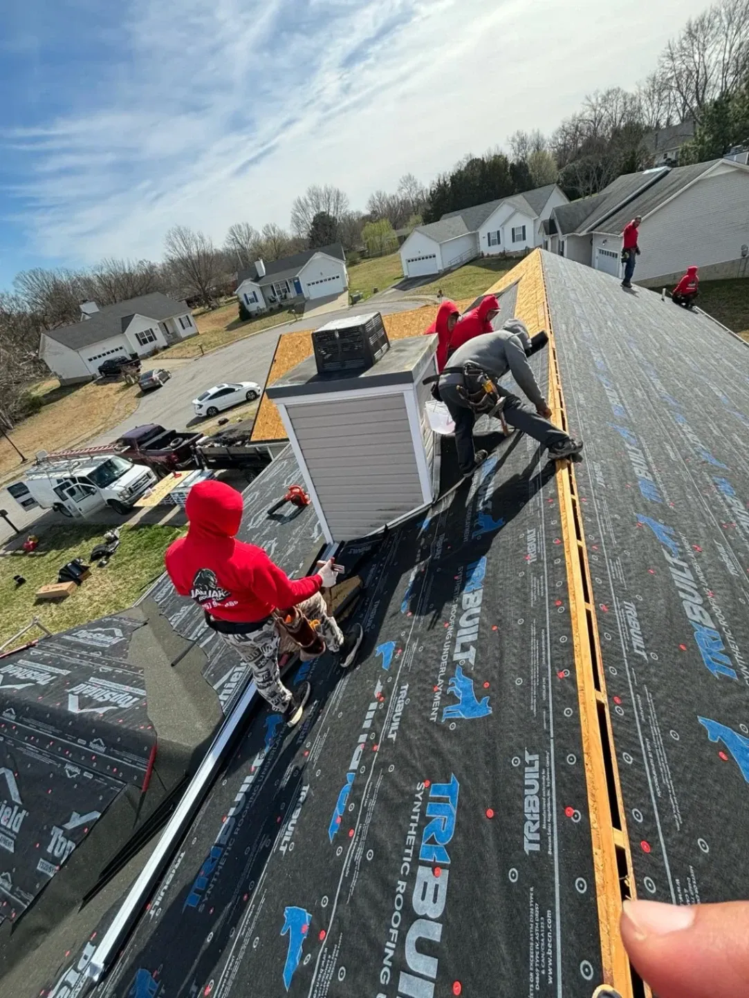 Roofing crew installing synthetic underlayment on a sloped roof of a suburban house on a sunny day.