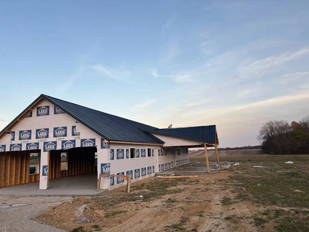 A single-story house under construction with a black metal roof and exposed wooden framework.