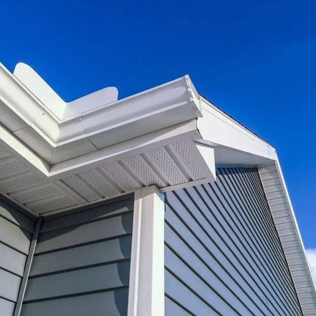 Close-up of a house exterior showing vinyl siding, soffit, and gutter under a clear blue sky