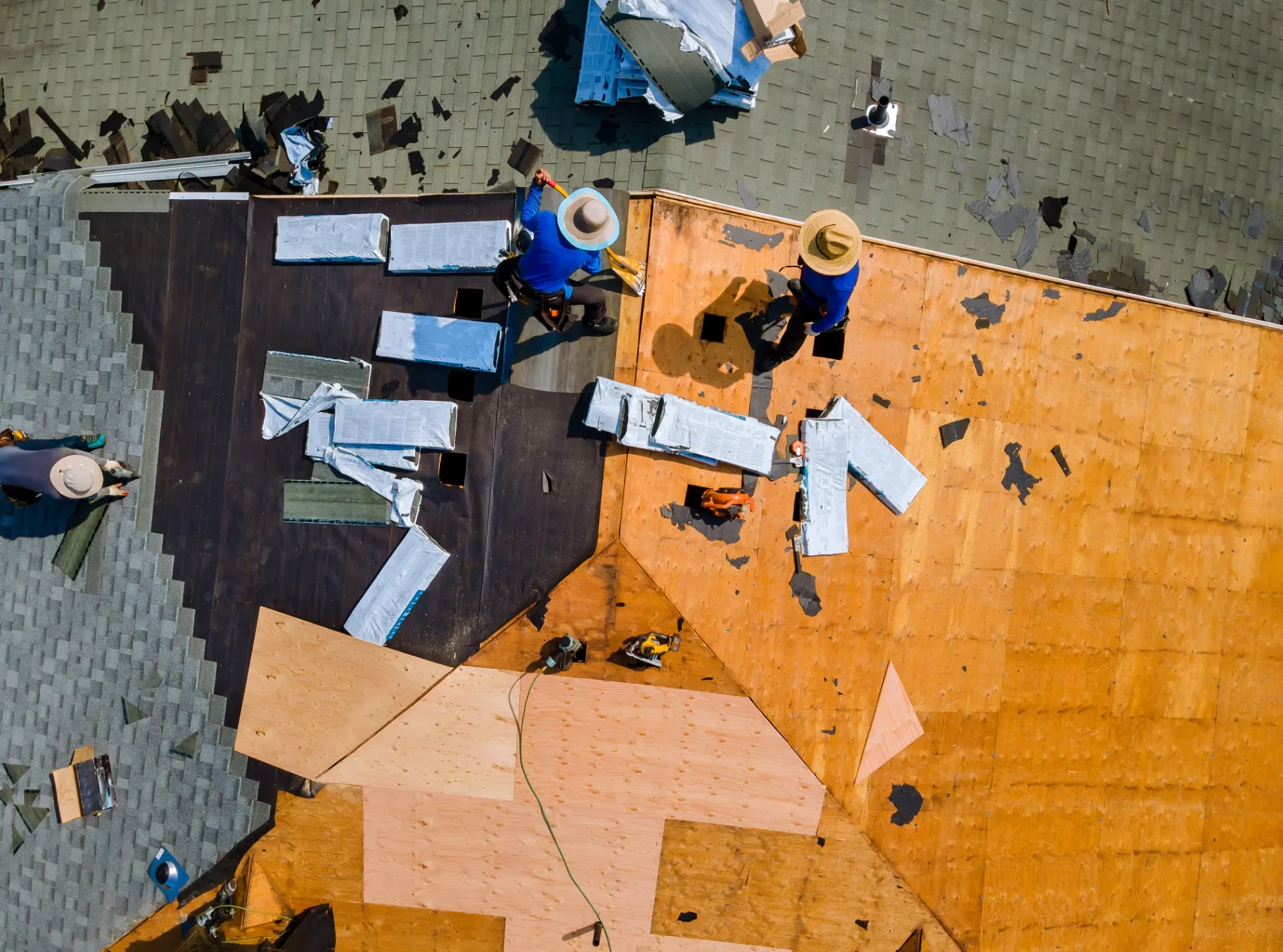 Aerial view of roof replacement in progress, with workers installing shingles over plywood and underlayment