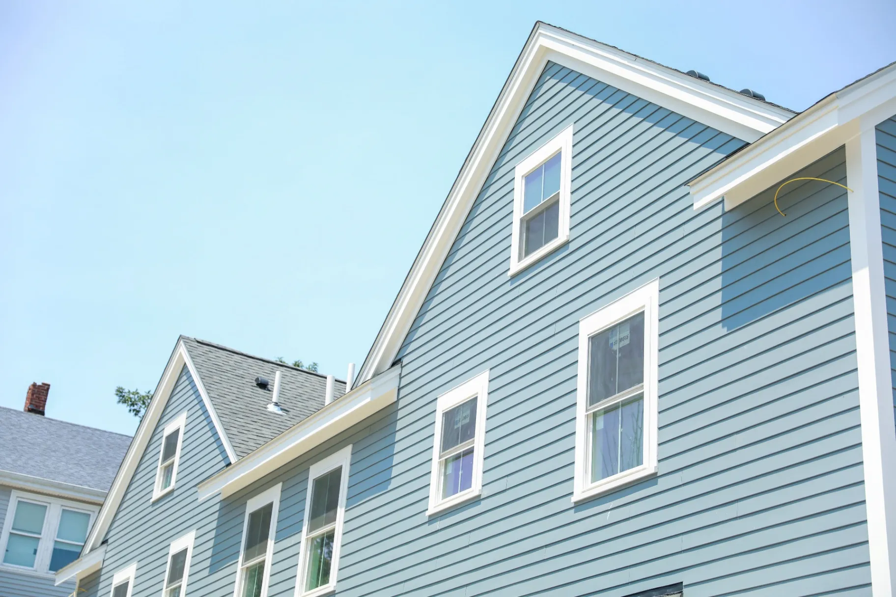 Two-story house with blue siding, white trim, and multiple windows under a clear sky.