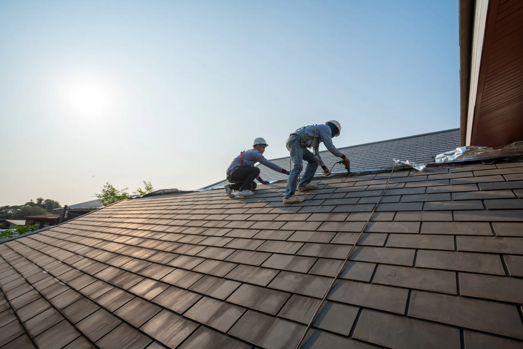 Roofer worker in special protective work wear and gloves using pneumatic gun and repair and replace roof tile on top of the new roof