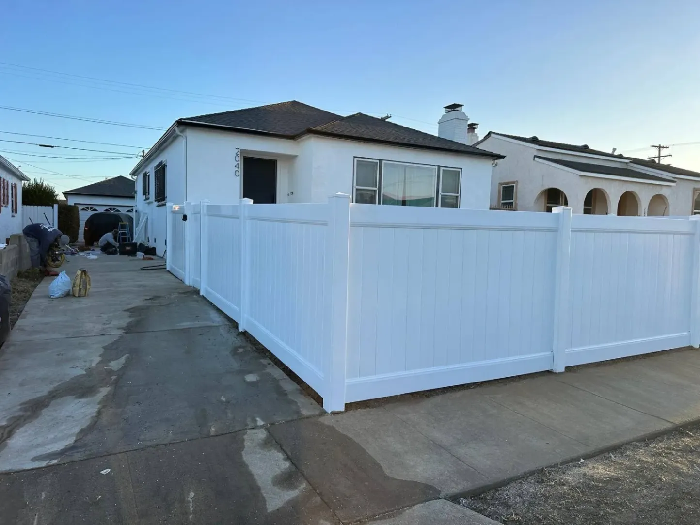 Single-story white house with a newly installed tall white vinyl privacy fence along the driveway and sidewalk.