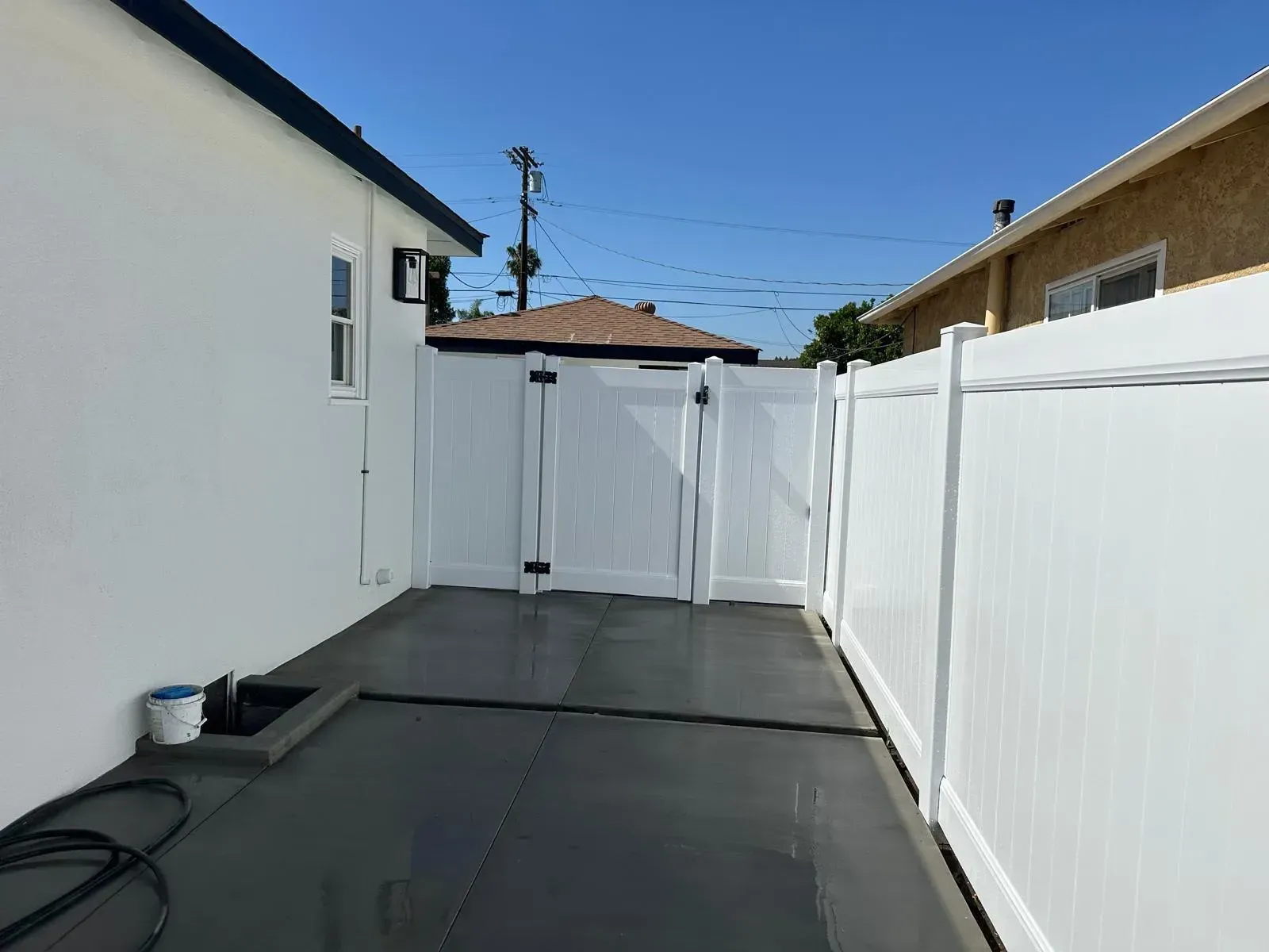 White vinyl privacy fence with matching gate installed along concrete side yard between houses.