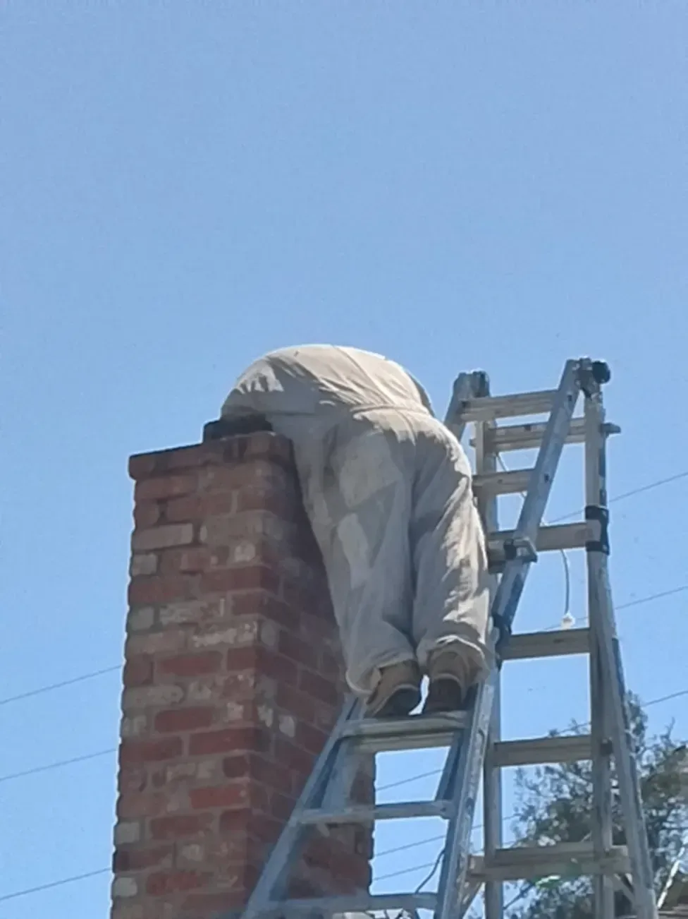 Professional technician performing live bee removal and relocation from a residential brick chimney in Atherton, CA, using a ladder and protective bee suit.