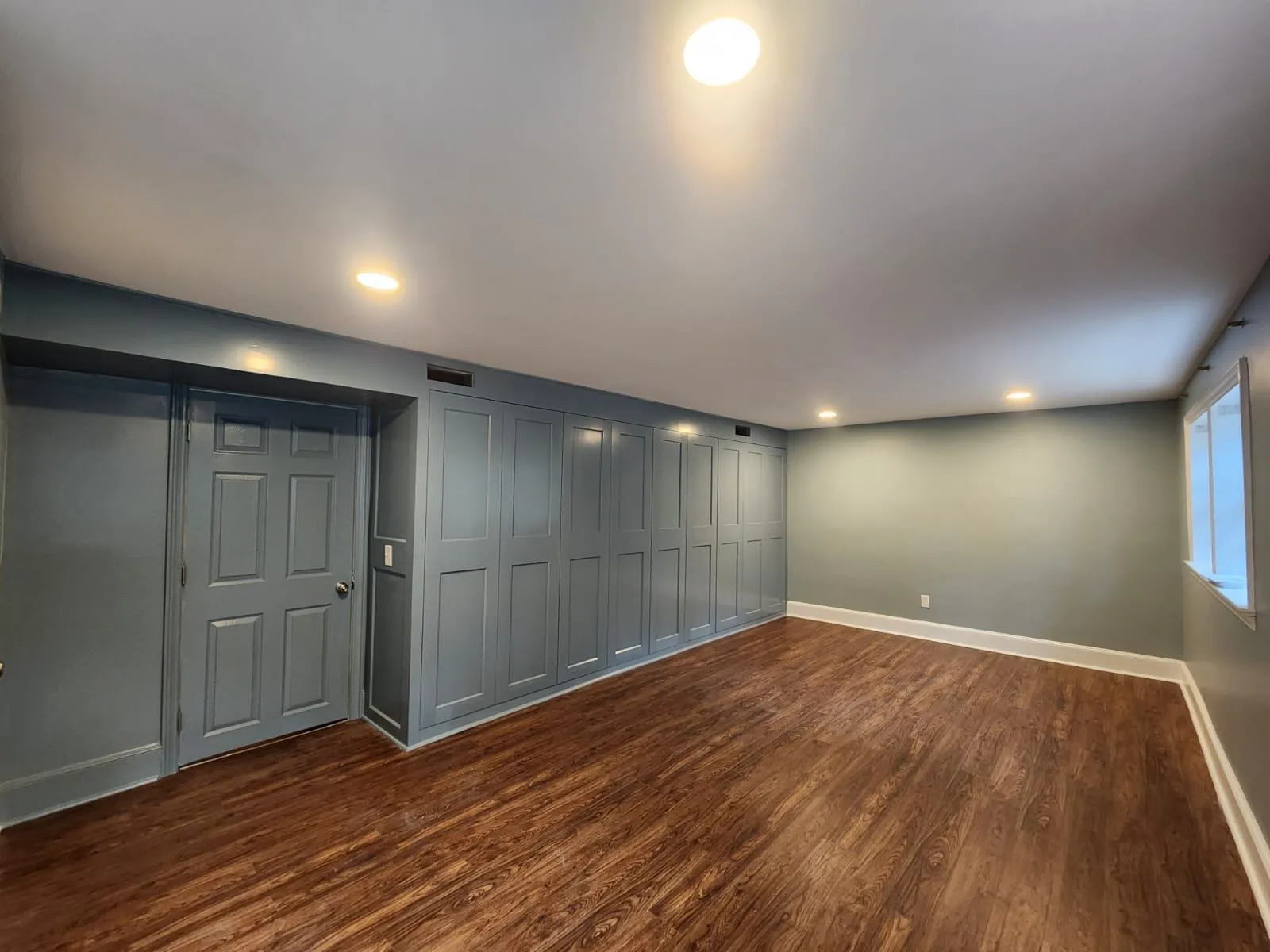 The image showcases a well-painted room with a sleek, modern design. The blue walls complement the rich wood flooring, creating a serene and stylish space. The neatly painted door and the detailed paneling on the wall enhance the overall aesthetic, making this a great example of an interior painting job.