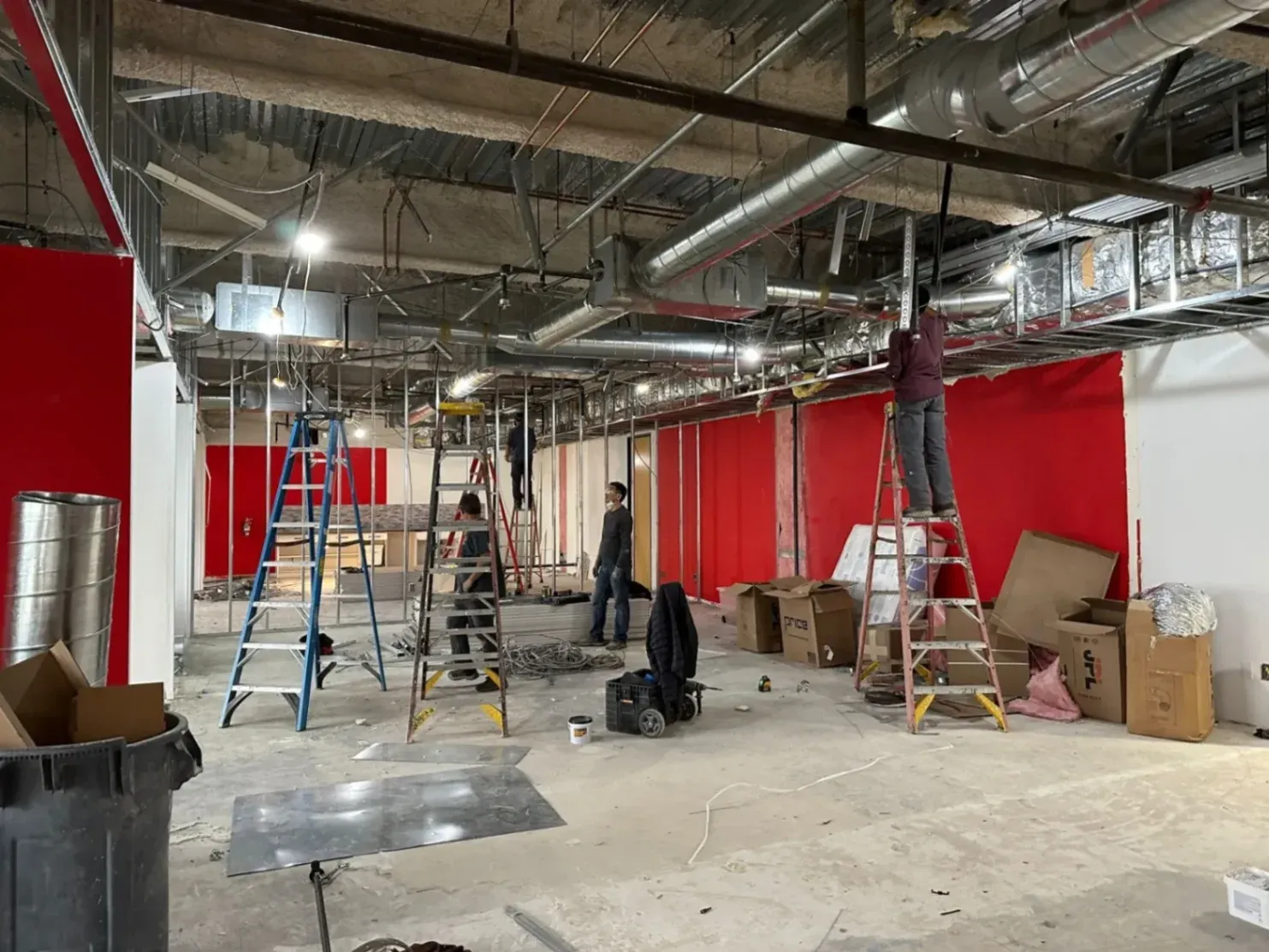 Several AAC Heating and Air technicians work on exposed ductwork and ceiling systems inside a commercial space under construction, showing a large-scale AC installation in Garden Grove, CA