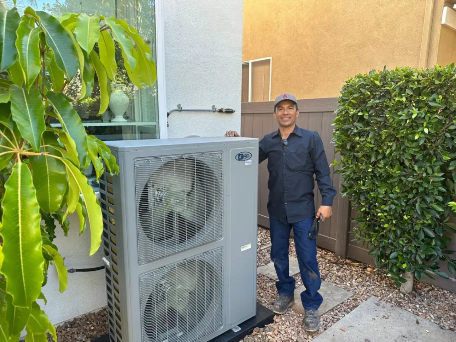 Angel Escobedo, owner of AAC Heating and Air, standing beside a newly installed AC unit in a residential setting.