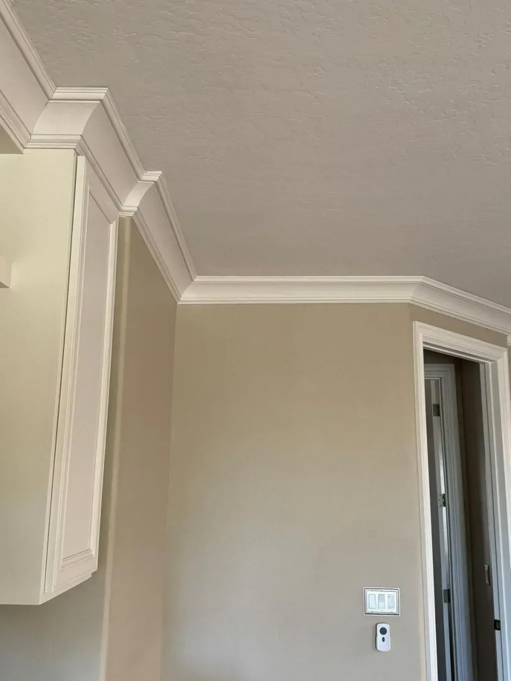 Crown molding installation featuring elegant, layered white trim that adds architectural detail where the beige walls meet the textured ceiling.