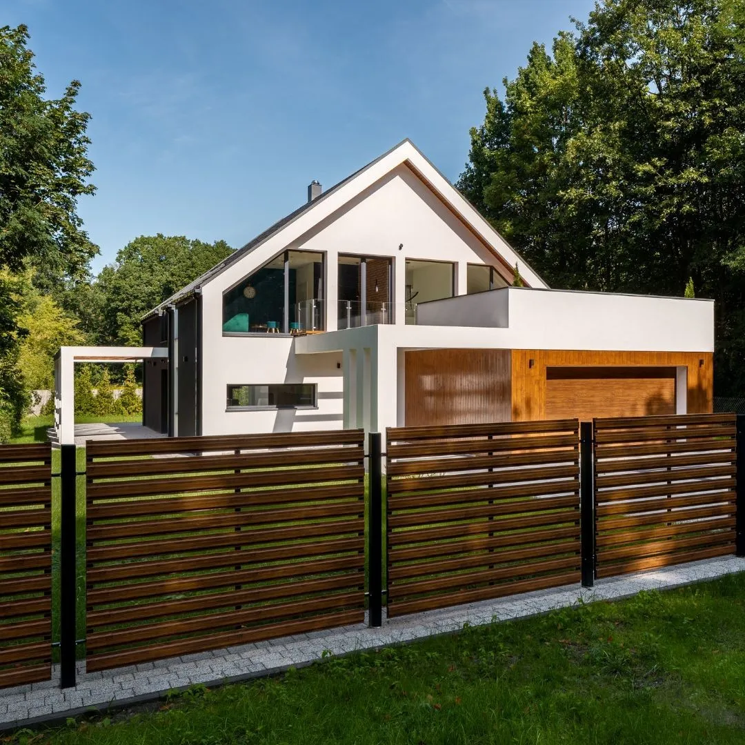 A modern two-story house with a white exterior and large windows, featuring a horizontal slatted wooden fence in the foreground