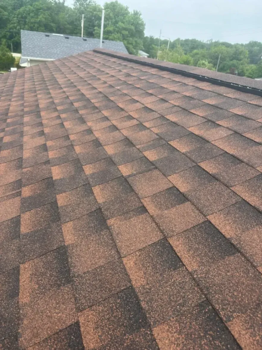 Close-up of newly installed, multi-toned brown and black architectural asphalt shingles on a residential roof with a ridge vent.