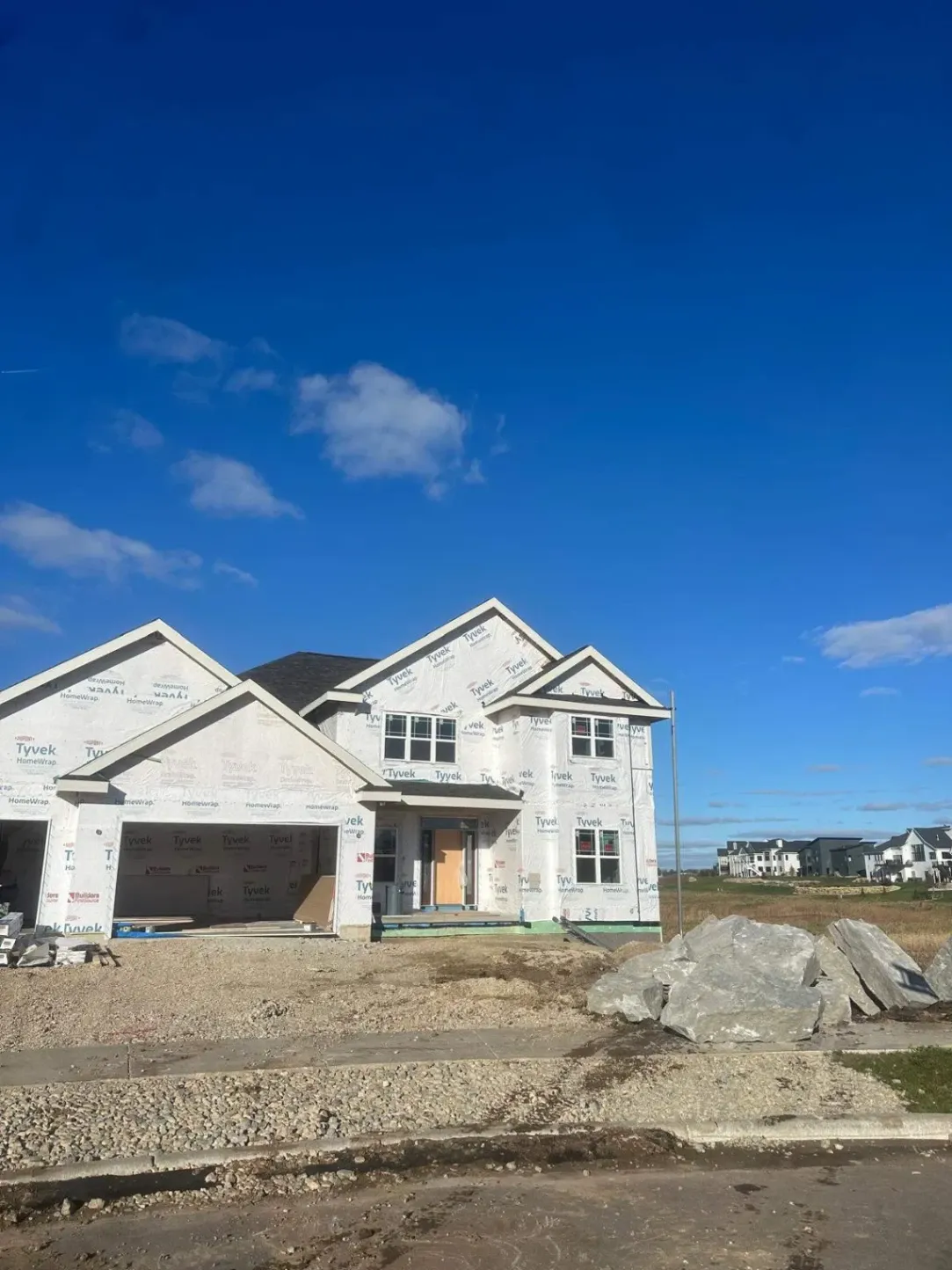 Two-story new construction home wrapped in Tyvek weather barrier with installed windows and front garage during residential siding installation process.