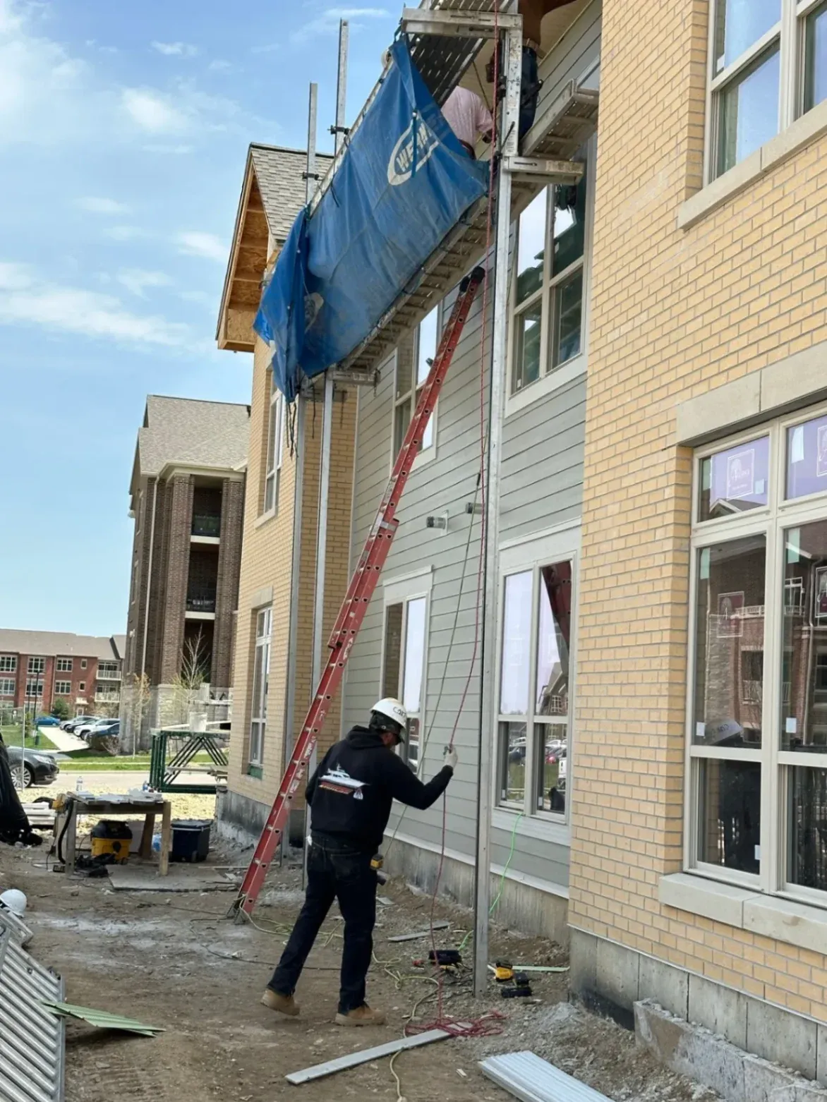 Construction worker operating scaffolding equipment during exterior siding installation on a multi-story residential building.