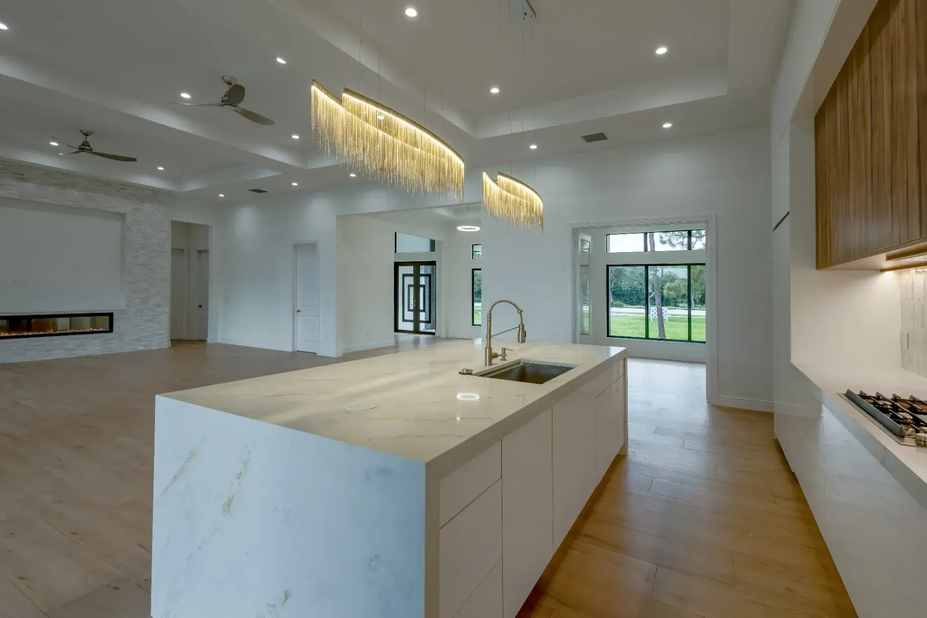 Modern and luxurious interior of a custom home in Marco Island built by Line Construction Inc. It features an open-concept kitchen with a marble waterfall island, elegant modern light fixtures, and wood accent cabinetry.