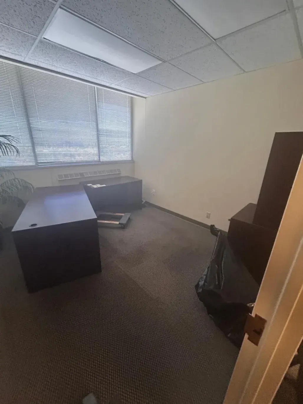 An empty corporate office room with large dark wood desks, a cabinet, and a trash bag being cleared out during a commercial junk removal service in Fairfield, CA.