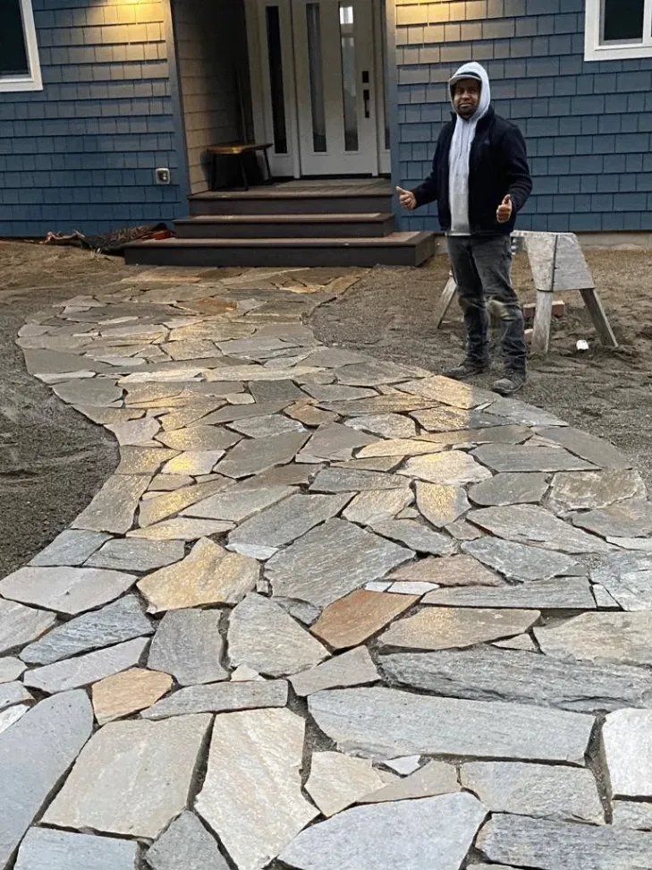 A man standing proudly next to a newly constructed stone pathway leading to the front entrance of a house with blue siding.