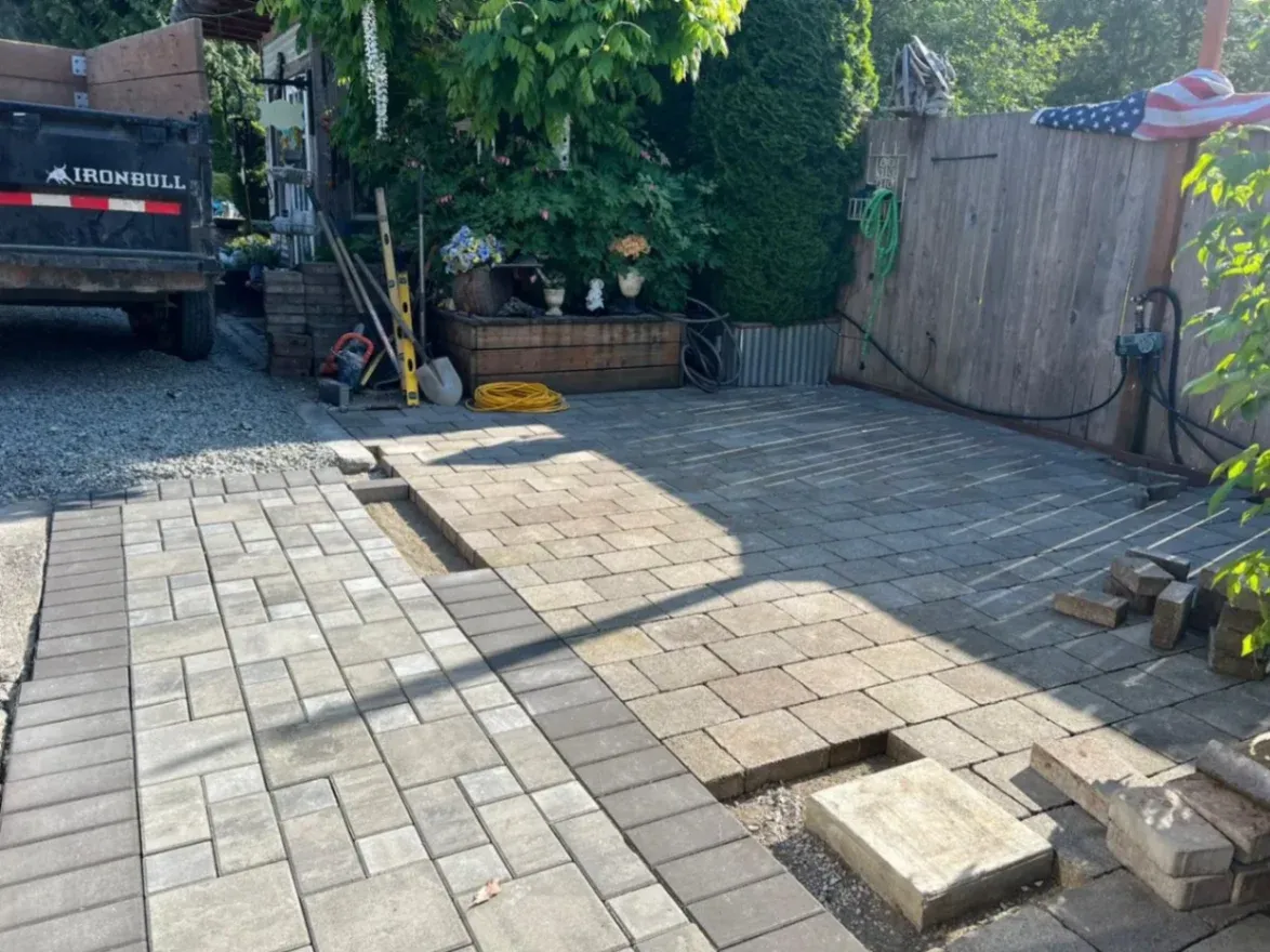 Worker installing a natural stone walkway in a Snohomish, WA backyard, surrounded by shrubs, garden tools, and a grassy lawn.