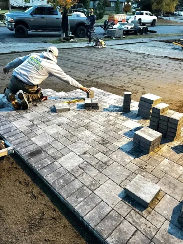Freshly installed stone paver patio with clean edges, surrounded by green lawn in a residential backyard, showcasing professional hardscaping by JMR Lawn Services.