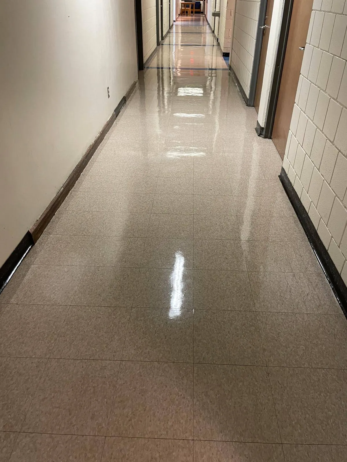 A long, empty hallway with shiny beige tiled floors, light-colored walls, and doors on both sides.