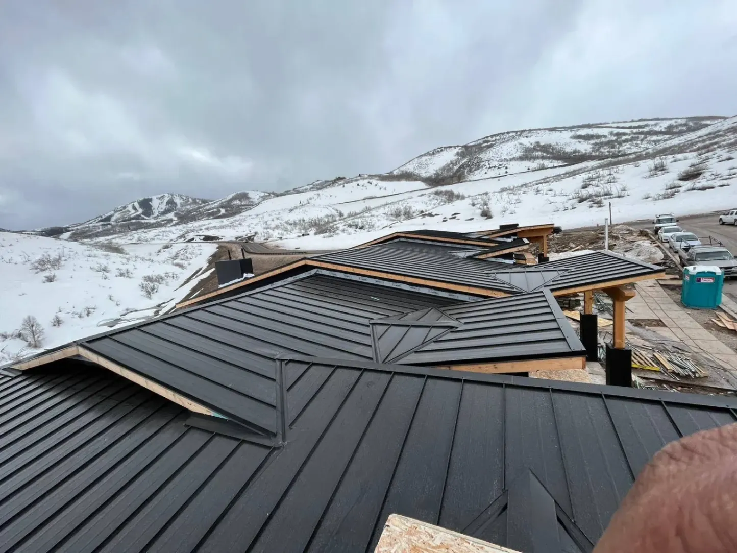 Black snap lock metal roof with clean seams on a modern home under construction in snowy hills.