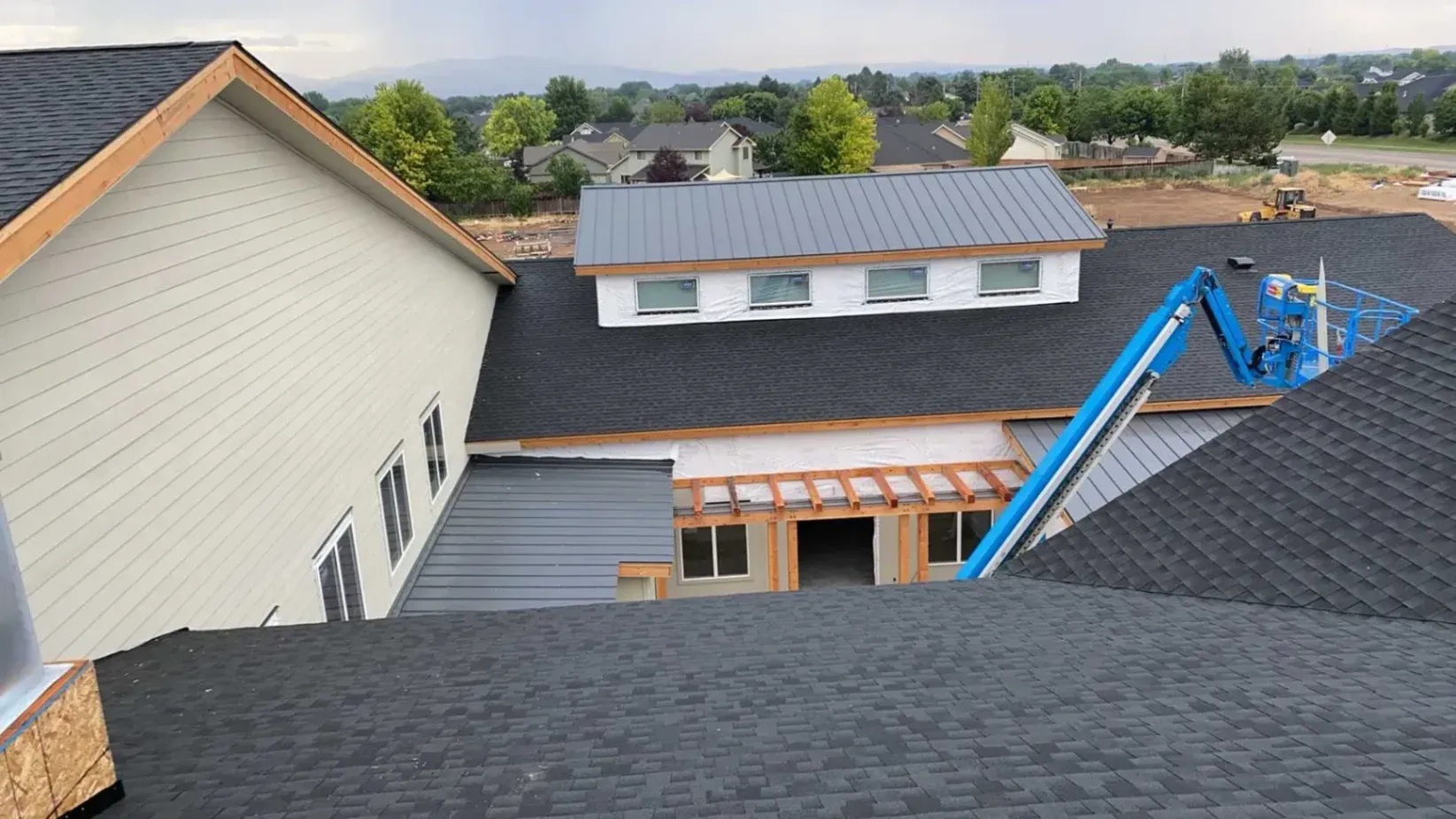 View of a residential roof featuring dark IKO shingles and a metal roofing section in the foreground, with construction equipment in the process of roof installation.