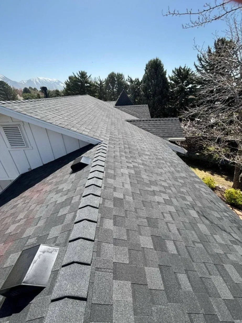 Close-up of new architectural asphalt shingles with ridge vent on a residential roof under clear sky.
