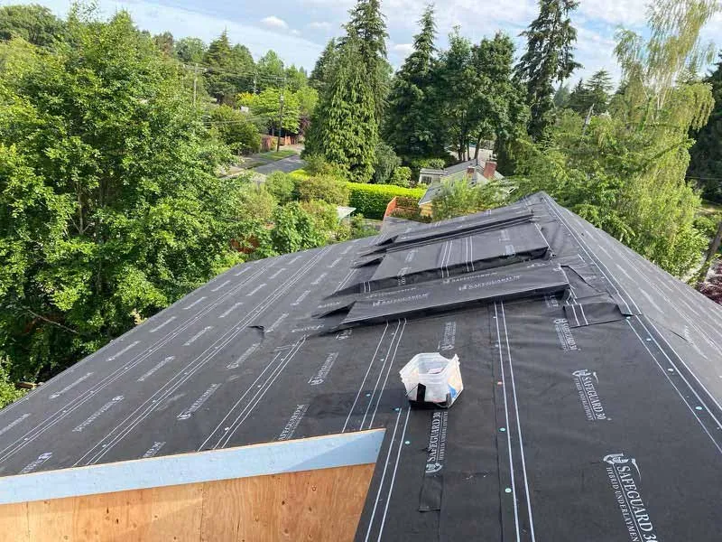 Roof with underlayment and skylight installation in progress, surrounded by trees.